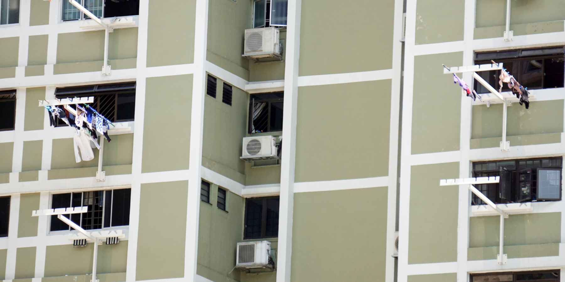 HDB block façade showing external air-conditioning units and laundry racks installed at windows.
